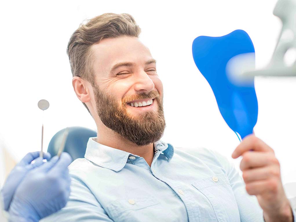 Hombre adulto sonriendo mirándose al espejo en el dentista